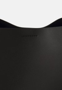 Czarna skórzana torba typu tote o gładkiej fakturze, z subtelnym przeszyciem wzdłuż górnej krawędzi i minimalistycznym designem.