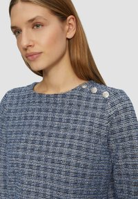 Blauer strukturierter Pullover mit einem gewebten Muster, Rundhalsausschnitt und drei metallischen Knöpfen an der linken Schulter. Weicher, gestrickter Stoff.