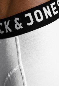 White elastic waistband with "Jack & Jones" in bold black text above snug white fabric, featuring contrasting stitching and a smooth texture.