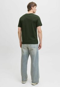 Grünes Baumwoll-T-Shirt mit kurzen Ärmeln, kombiniert mit hellblauen weit geschnittenen Jeans, die zwei Gesäßtaschen und subtile Verblassungen aufweisen.