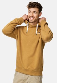 Bluza z kapturem w musztardowym kolorze, z kieszenią typu kangur, białymi i szarymi sznurkami, miękką teksturą, logo na piersi oraz ściągaczami na rękawach.