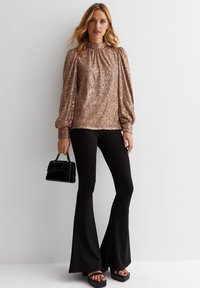 Sparkly rose gold top with puffed sleeves, gathered neckline, paired with black flared pants and black handbag, featuring platform sandals.