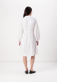 Rochie albă, respirabilă, cu broderie, talie elastică și mâneci tip balon. Pur tată cu pantofi negri, cu talpă joasă, arătând un design simplu și curat.