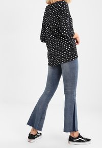 Haut noir à motifs avec des formes triangulaires blanches, assorti à un jean flare bleu clair avec des fentes latérales, et des baskets noires.