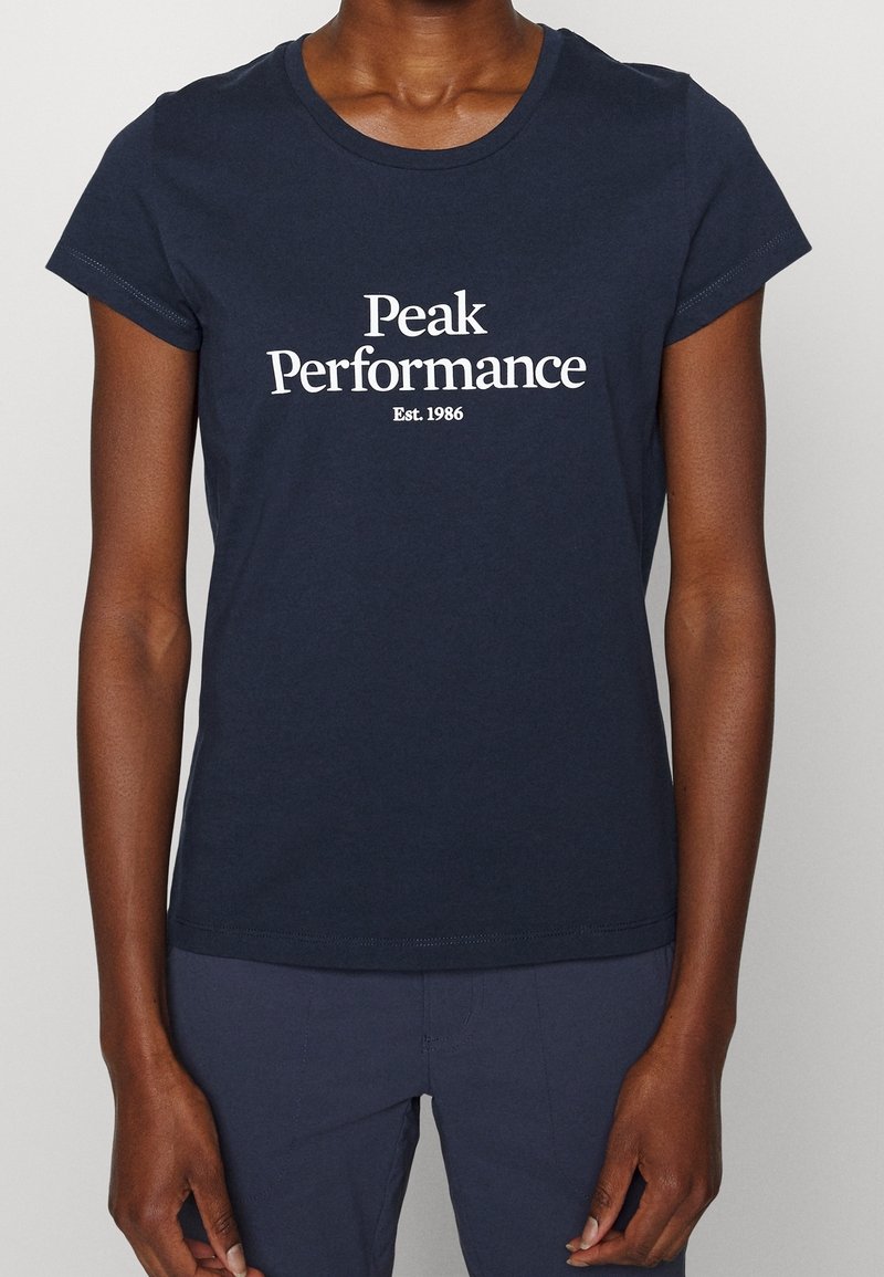 Námořnická modrá bavlněná tričko s krátkým rukávem, s bílým textem "Peak Performance" a "Est. 1986" ve středovém, pohodlném písmu.