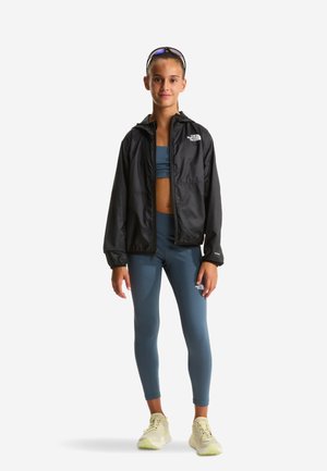 Sort letvægtsjakke med hætte, kombineret med en mørk grønblå top og leggings. Outfittet har The North Face-logoer og atletiske sko.