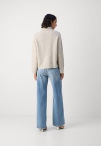 Kremfarget, ribbet strikket genser med høy krage, kombinert med lyseblå, vide jeans. Modellen har på seg hvite hælsandaler.