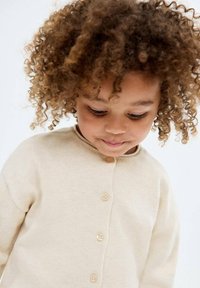 Cardigan bej din tricot cu guler rotund  și închidere cu nasturi, având o textură moale și mâneci lungi, potrivit pentru copii.