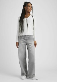 Pull blanc à col en V associé à un jean large gris clair. La tenue présente une coupe décontractée et un design minimaliste, complétés par des baskets blanches.