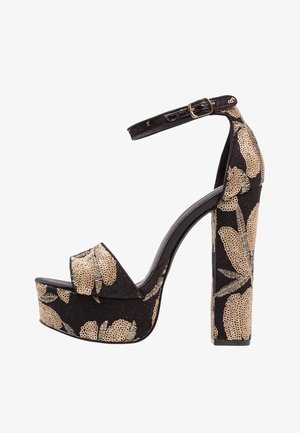 Zapatos de tacón negro con plataforma y patrón floral dorado, con un tacón alto grueso y una correa en el tobillo con un hebilla. Suela antideslizante.