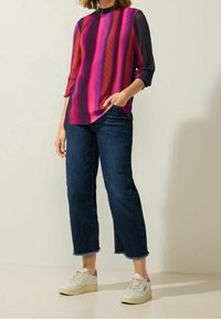 Kleurrijke gestreepte blouse in tinten roze en paars, gecombineerd met donkere denim wijde broeken en witte sneakers. Gladde, gestructureerde stof.