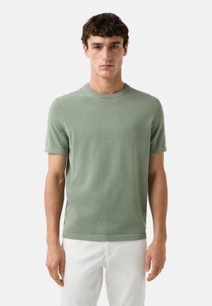 Lys grøn kortærmet strik T-shirt med rund hals, blød tekstur og oprullede ærmer, parret med hvide bukser.
