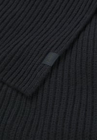 Sort ribbet strikstof med en blød tekstur, der har et lille sort mærke med linjemønster. Det overordnede design er enkelt og monochromt.