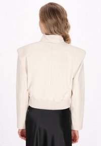 Cremfarvet læder cropped jakke med skulderpuder. Har en høj krave og ribbet kant. Glat tekstur, minimalistisk design.
