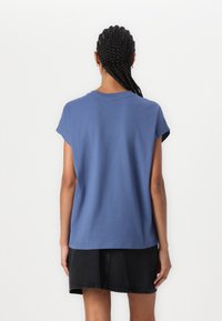 Blaues Baumwoll-T-Shirt mit kurzen Ärmeln, Rundhalsausschnitt und lässiger Passform, kombiniert mit einem schwarzen Jeansrock, der am unteren Rand sichtbar ist.