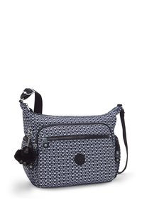 Bolso cruzado de patrón en blanco y negro con correa ajustable, bolsillo frontal con cremallera, cremalleras laterales y un pequeño llavero de mono de peluche negro adjunto.
