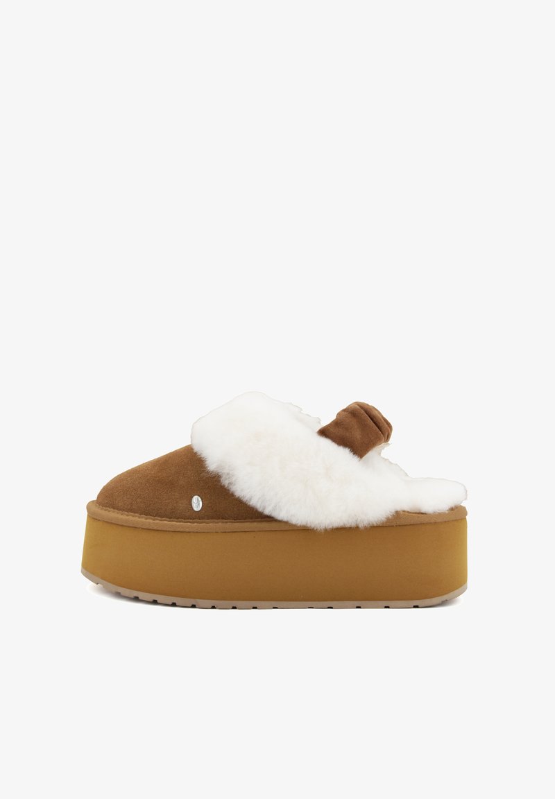 Pantofole in suede marrone con una foderatura in pelliccia sintetica bianca, suola piatta e punta arrotondata. Presenta un nodo decorativo sulla parte superiore.