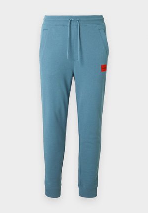 Világoskék melegítőnadrág húzózsinóros derékkal, oldalzsebekkel és egy piros logófelvarróval a bal csípőnél. Bordázott szegély a bokáknál.