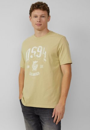 Beżowy t-shirt z krótkim rękawem, wykonany z bawełny, z białym wzorem graficznym i tekstem z przodu oraz okrągłym dekoltem. W połączeniu z ciemnymi dżinsami.