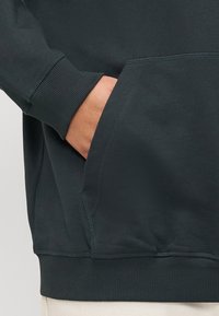 Felpa verde scuro realizzata in morbido cotone misto, con polsini e orlo a costine, tasca a marsupio e dettagli di cucitura piatta sulle cuciture.