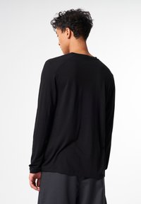 Schwarzes Langarm-T-Shirt mit Rundhalsausschnitt, weichem Material und Raglanärmeln, kombiniert mit grauen Hosen, von hinten betrachtet.