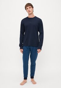 Camisa de manga longa azul-marinho com logótipo em relevo, combinada com calças de pijama azuis estampadas, apresentando um subtil design geométrico e punhos nos tornozelos.