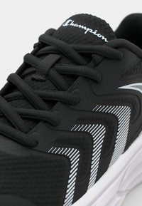 Baskets de sport noires avec un upper texturé, logo Champion blanc et un motif en chevron distinctif en noir et blanc.