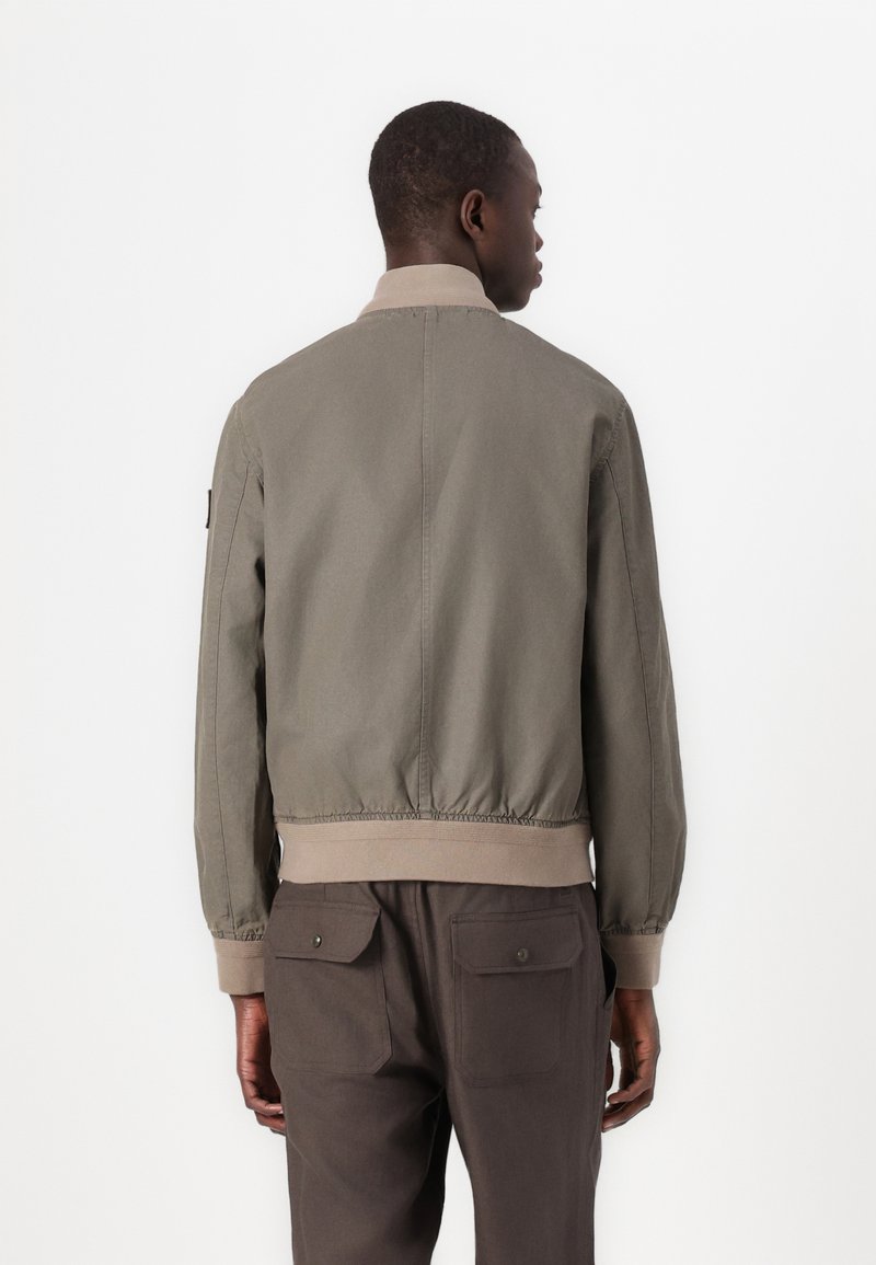 Giacca bomber color khaki con colletto e polsini a coste crema, vita elastica e due tasche posteriori con patta. Finitura liscia e opaca.