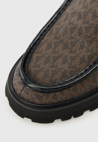 Καφέ μπότες με σχέδιο, από υλικό συνθετικό με υφή, μαύρες λεπτομέρειες και παχιά καουτσούκ σόλα με ανάγλυφο σχέδιο για πρόσφυση.