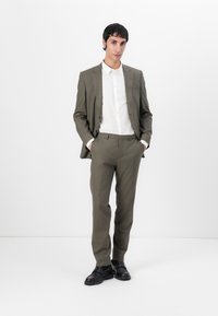 Olive green suit with a fitted blazer and straight-leg trousers, paired with a white button-up shirt and black shoes. Smooth texture.
