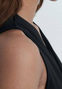 Haut sans manches noir avec un design lisse et ajusté et un décolleté incurvé, mettant en valeur les épaules et le haut des bras.