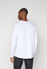 Long-sleeve white shirt, round neckline, smooth texture, side slits at hem, paired with fitted black leggings.