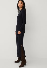 Marineblå ribbet kjole med lange ærmer, krave, sideslids og tætsiddende silhuet, parret med brune ruskinds knæhøje støvler.