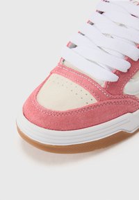Low-top sneaker featuring a pink suede upper, cream toe box, white laces, and a gum rubber outsole with textured detail.