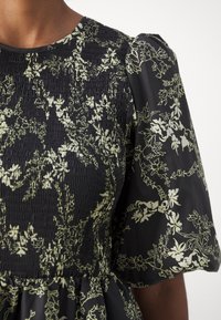 Gros plan d'une robe noire avec corsage froncé et manches courtes bouffantes à motif floral clair.