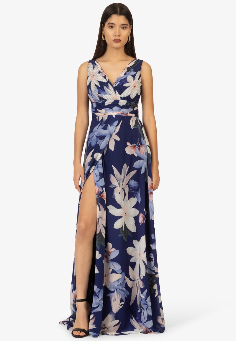 Abito lungo blu navy con un motivo floreale in colori chiari. Ha un design avvolgente con uno spacco profondo e spalline sottili. Abbinato a sandali neri.
