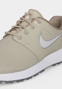 Μπεζ αθλητικό παπούτσι Nike με λευκό λογότυπο swoosh, μπεζ κορδόνια, επενδυμένο κολάρο και υφασμένο λευκό πέλμα με ορατό μαύρο πέλμα.