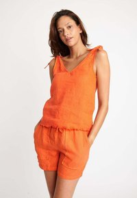Canottiera arancione in lino con scollatura a V e spalline annodate, abbinata a pantaloni corti coordinati con cordoncino e tasche frontali.