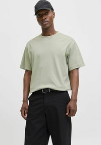 Tricou din bumbac verde deschis, cu mâneci scurte, asortat cu pantaloni negri și o pălărie de baseball neagră, având un croi lejer și un design simplu.
