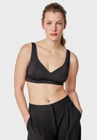 Soutien-gorge noir sans coutures avec des larges bretelles, un décolleté en V et une texture lisse. Associé à un pantalon noir taille haute.