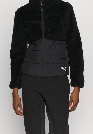 Schwarze Fleecejacke mit gesteppter Mittelpartie und weißem Puma-Logo unten rechts, getragen mit passenden Fleecehosen.