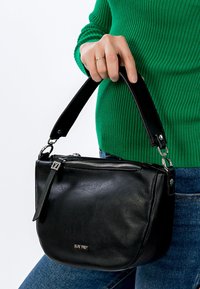 Czarna skórzana torebka o zaokrąglonym kształcie, zamykana na zamek błyskawiczny, z krótkim czarnym uchwytem. Ma niewielkie logo i fakturowaną powierzchnię.