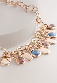 Gold-toned chain bracelet with multiple hanging charms featuring glossy colored stones in blue, brown, and metallic finishes.