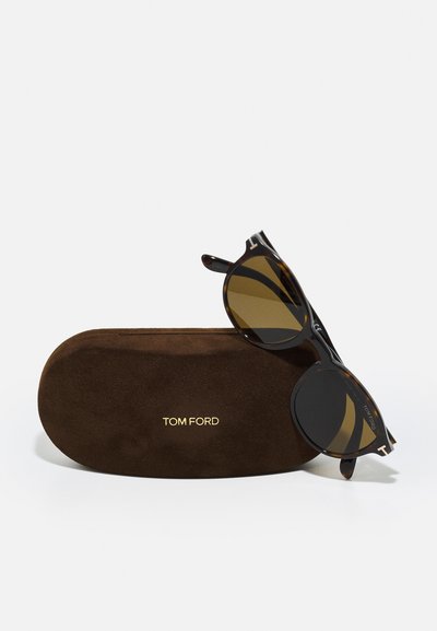 Ochelari de soare rotunzi, cu carapace de țestoasă maro și lentile întunecate, având accente aurii. Împreună cu un toc din suede maro, cu inscripția "TOM FORD" embosată.