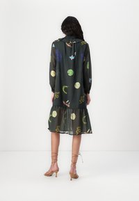 Robe transparente vert foncé à manches longues et ourlet froncé, ornée de motifs colorés d'animaux et de plantes.