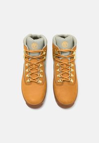 Botas de senderismo de cuero marrón con puntera reforzada, herrajes dorados y un cuello acolchado gris, que presentan cordones amarillos a contraste y un logo.
