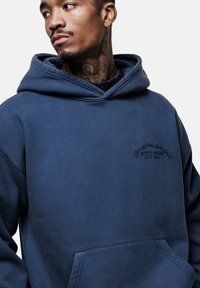 Felpa con cappuccio blu navy, dotata di tasca frontale, texture morbida e logo ricamato sul petto. Presenta una vestibilità classica e rilassata.