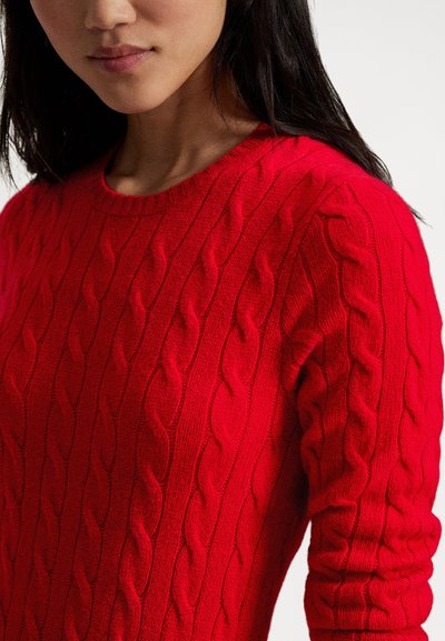 Rdeč pulover z vzorcem kabelskega pletenja, okrogel izrez, teksturirana površina in oprijete rokave, prikazan na modelu od prsnega koša navzgor.