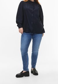 Blusa navy con cuello volante y botones al frente, combinada con jeans skinny azul claro y mocasines negros de plataforma. Textura de tela suave.