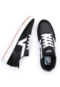 Svarte sneakers med hvite detaljer, teksturert stoff, glatt lær, gummisåle og fremtredende side-logo. Har hvite snøringer og en støttende design.